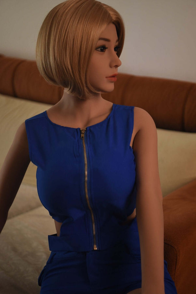 Blonde Liebespuppe Smilla mit blondem Bob, blauem Kleid, mit atemberaubend, tiefem Ausschnitt flirtet auf Sofa